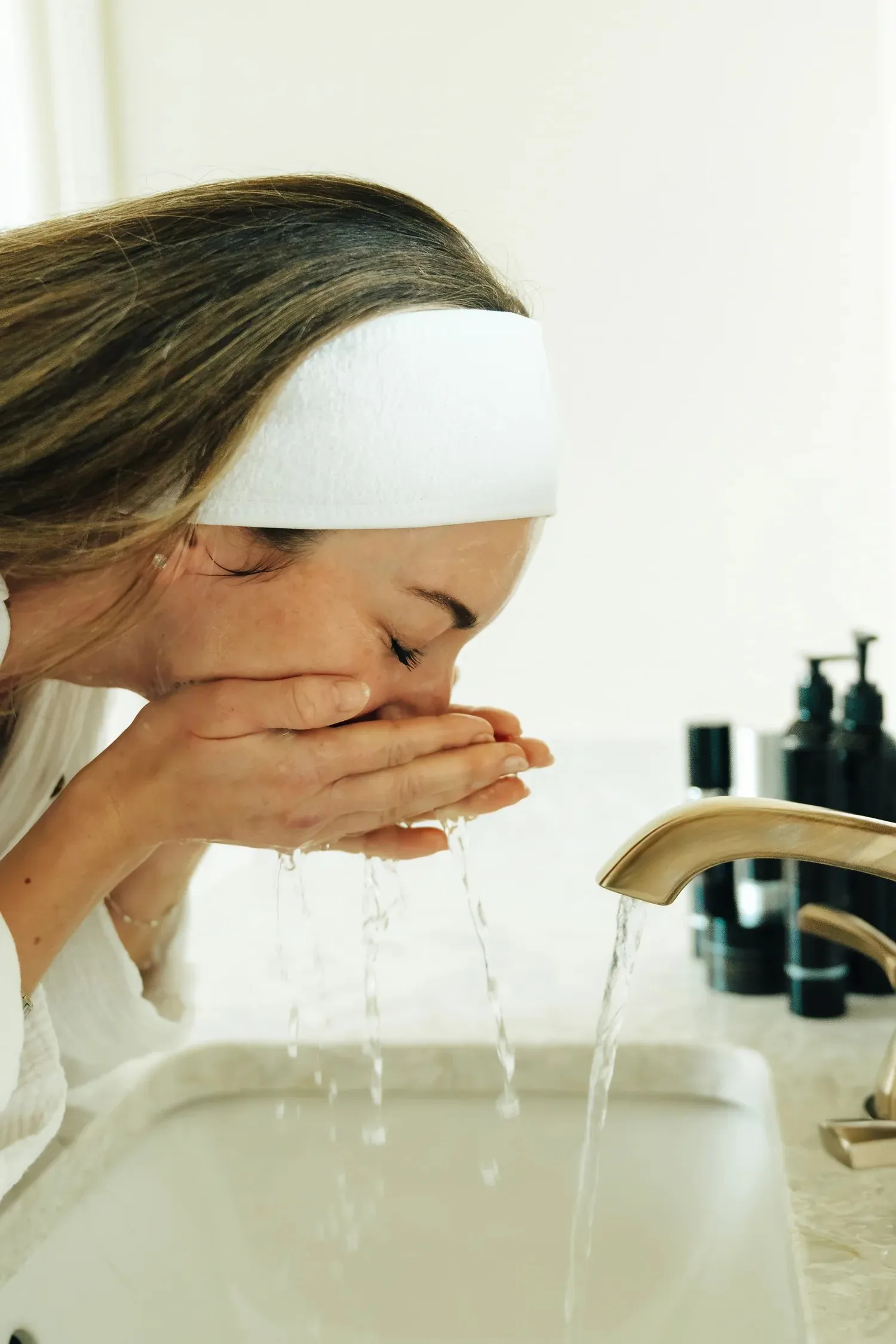 Woman cleansing face at sink with CFC products